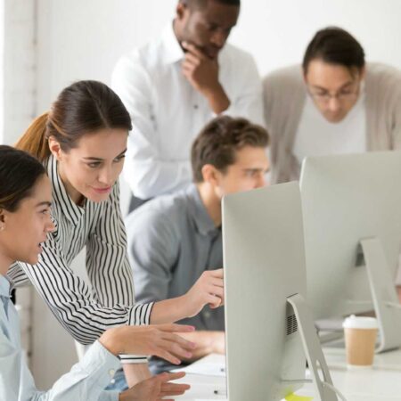 Executive mentor explaining intern or new employee online task pointing at computer screen, female boss supervisor teaching young girl to use corporate software or helping with difficult assignment